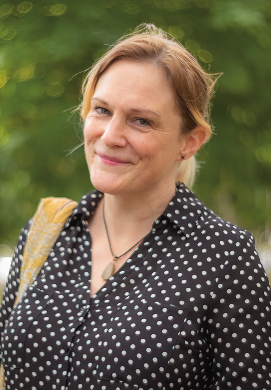 K. Elizabeth Stevens, grinning outside, wearing a polka-dotted shirt and necklace