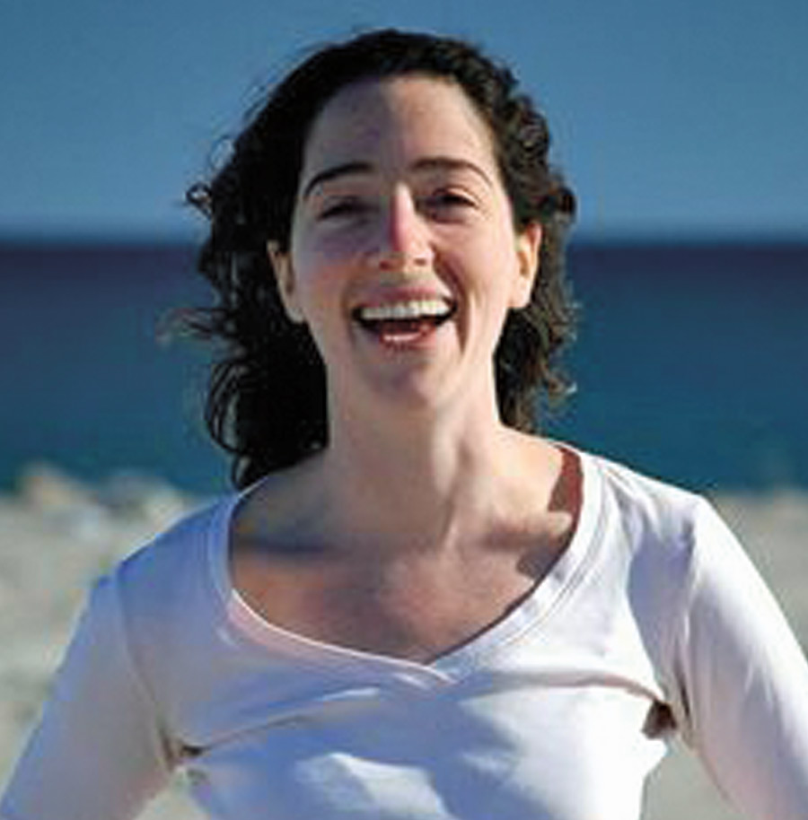 Closeup of smiling Leah Zallman, outside in the sun with water behind her