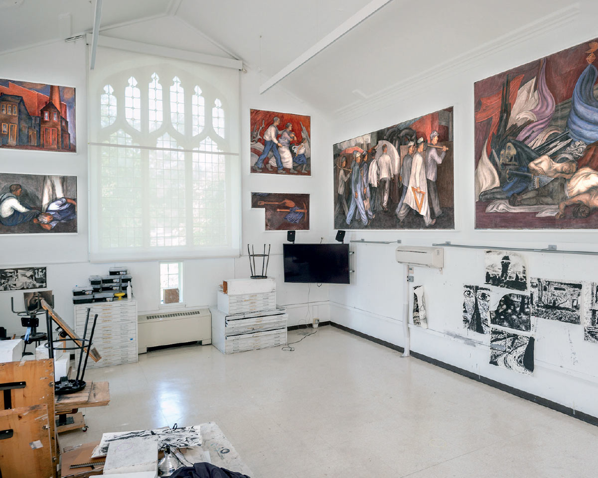 An art studio space with a large Gothic-style window, fresco paintings lining the white walls