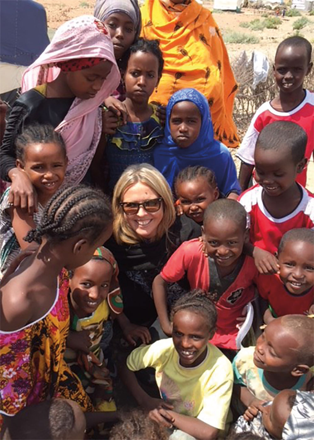 Allison Oman Lawi smiling in sunglasses surrounded by smiling children