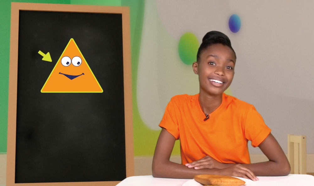 TV screen shot, girl smiling with hands on table, beside blackboard with triangular cartoon face
