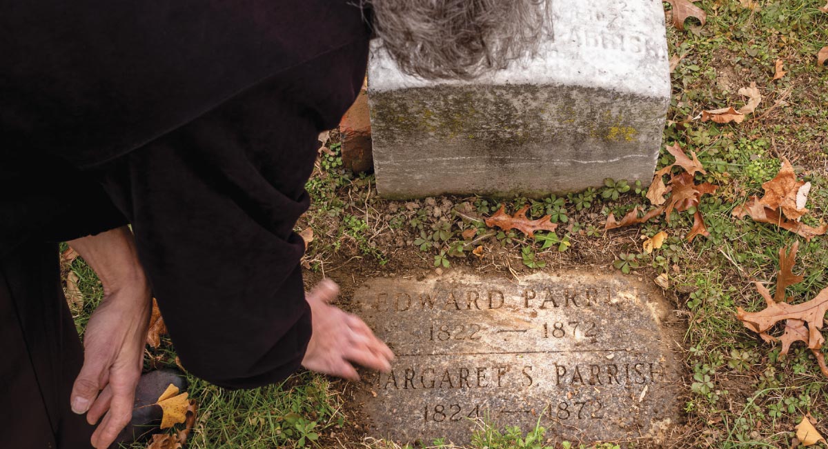 A woman’s hand touching the burial marker for Edward Parrish and Margaret Parrish. 
