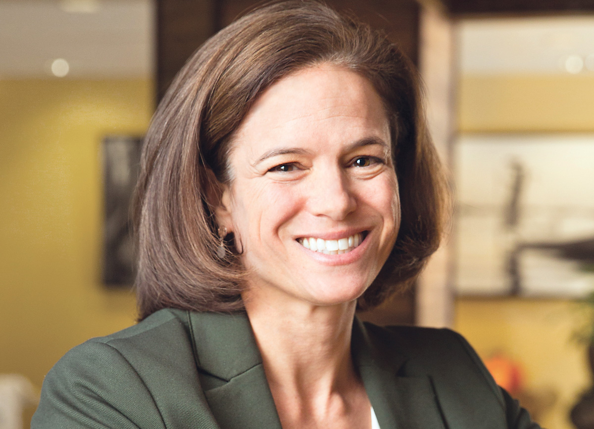 Rebecca Katz smiling in a headshot. She has shoulder-length brown hair and is wearing an olive-colored suit jacket.