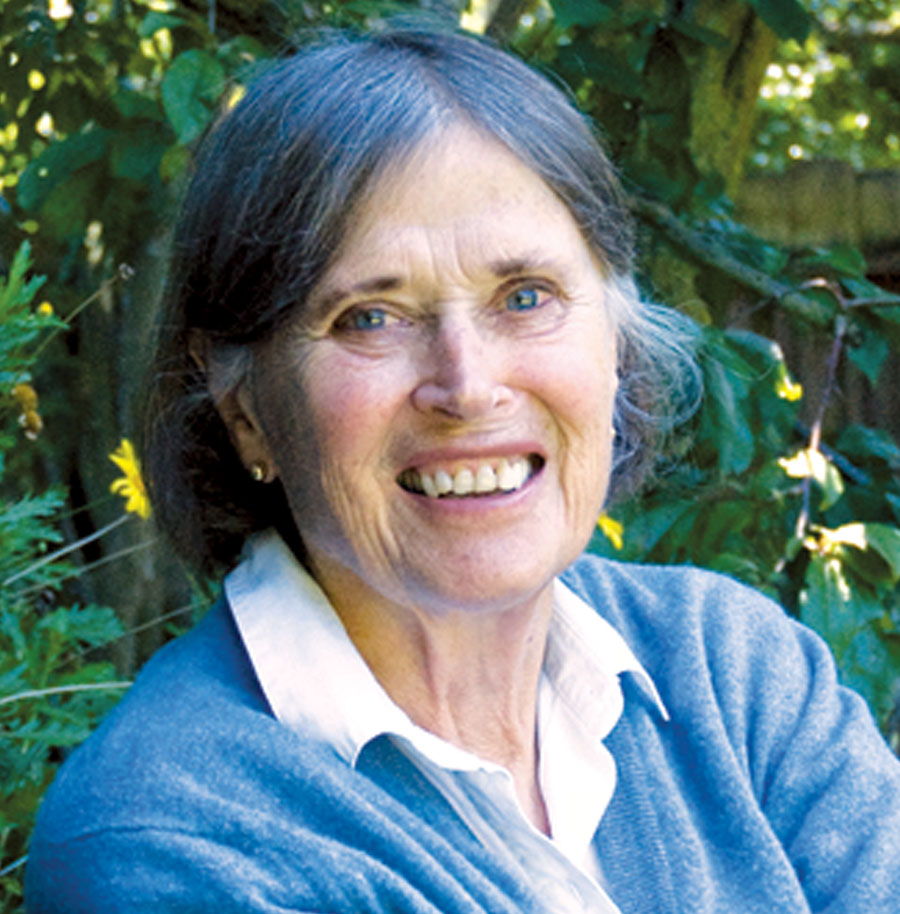 Joy Kaiser, smiling and sitting outside, wearing a white collared shirt and blue sweater