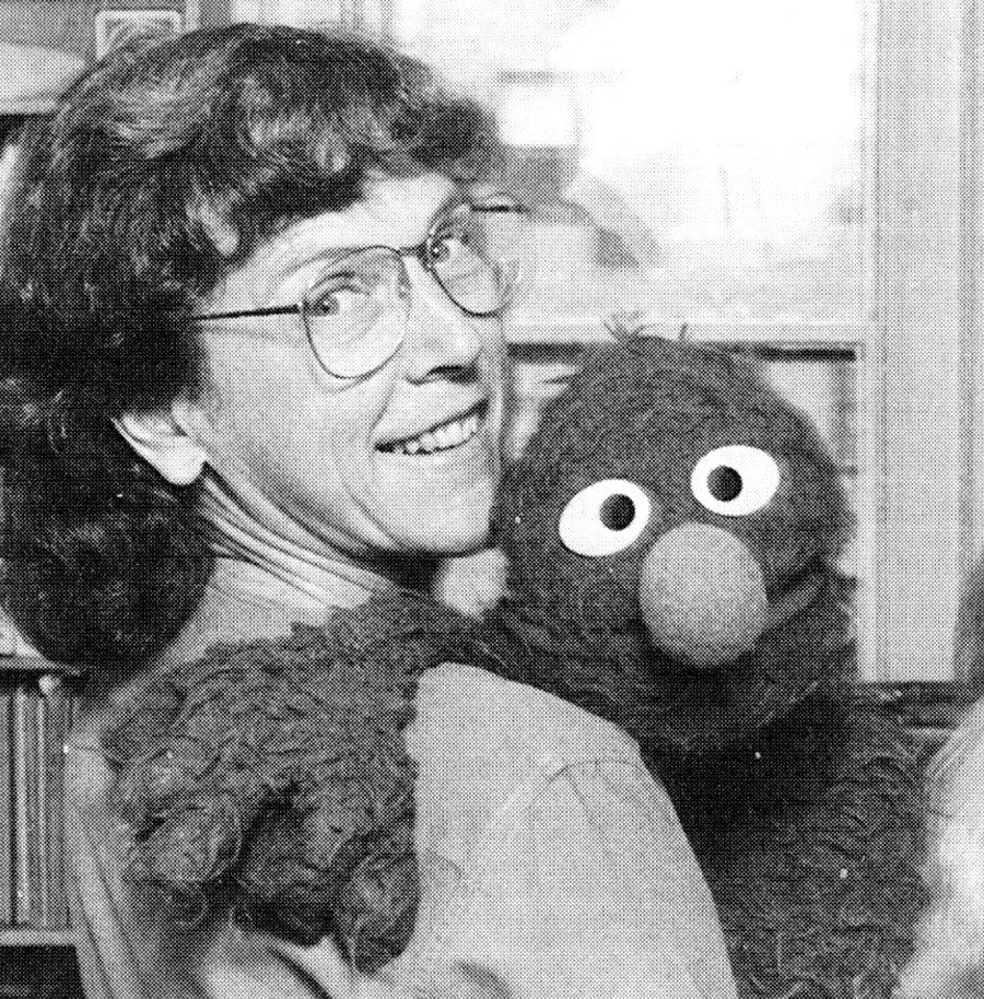 Black-and-white headshot of Caroly Wilcox, looking over her shoulder while holding the muppet Grover