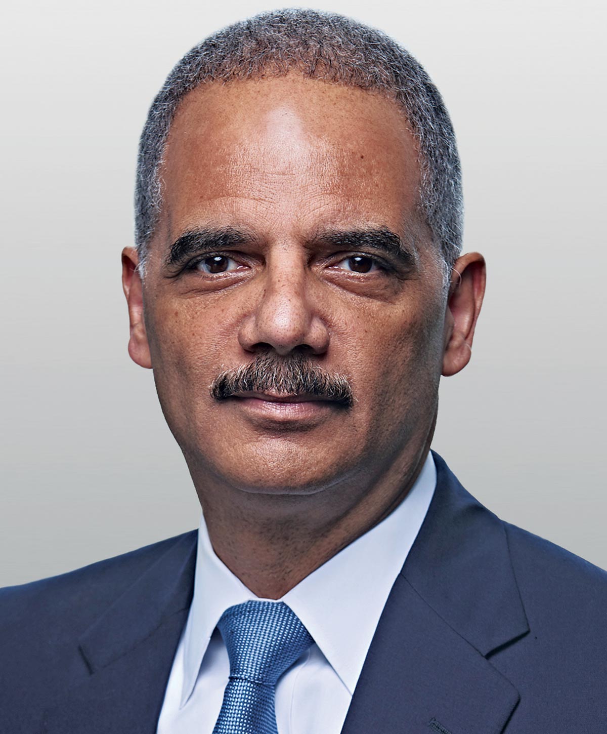 Headshot of Eric Holder wearing a suit with a blue tie