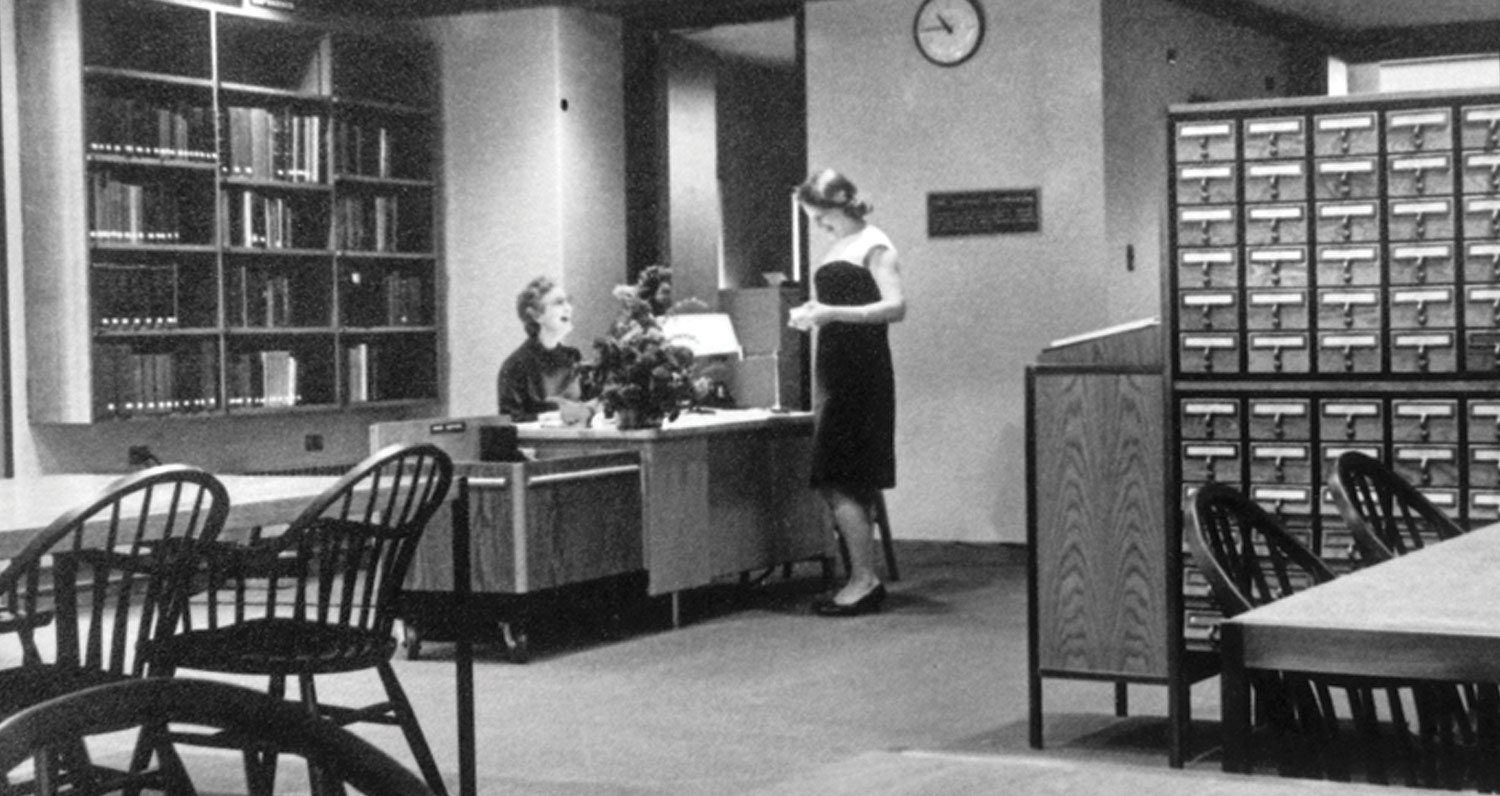 Black-and-white image of Friends Historical Library, with two women smiling and talking, wearing 1960s-era clothing