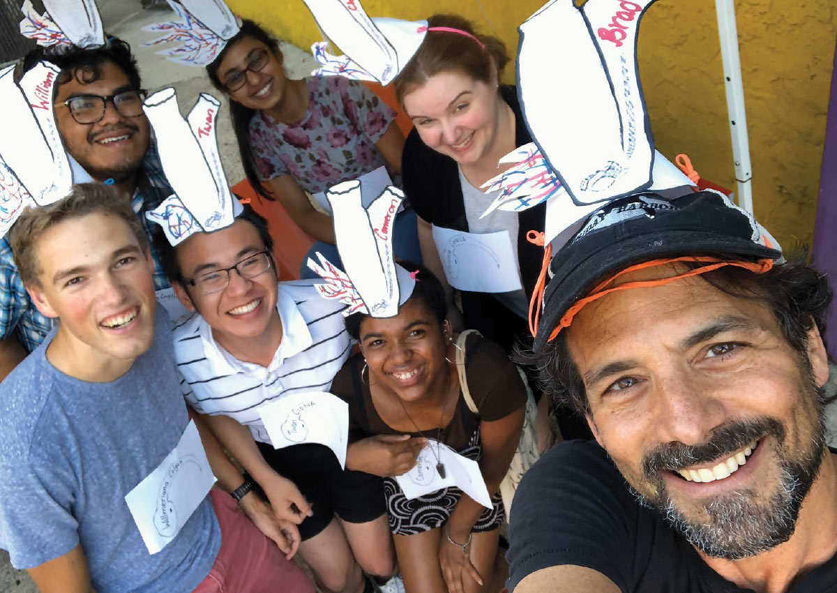 Bradley Davidson smiling with a group of students and a postdoctoral researcher. They’re all wearing white paper sea squirt hats with their names on them.