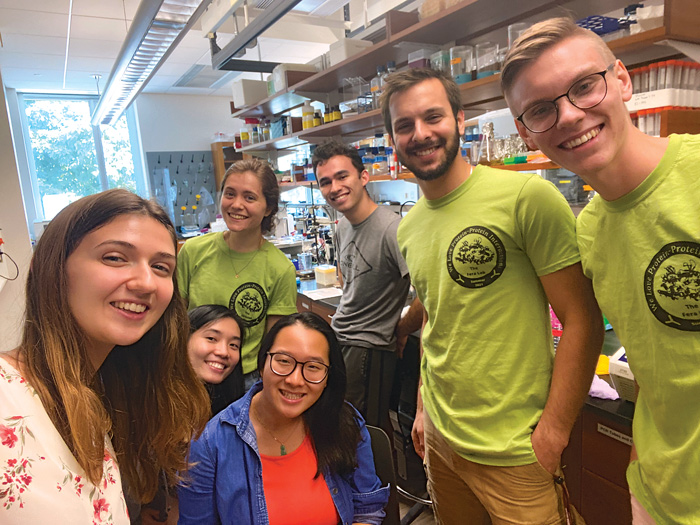 Daniela Fera in a lab with six smiling students. Three of them are wearing lime-green “Fera Lab” shirts.
