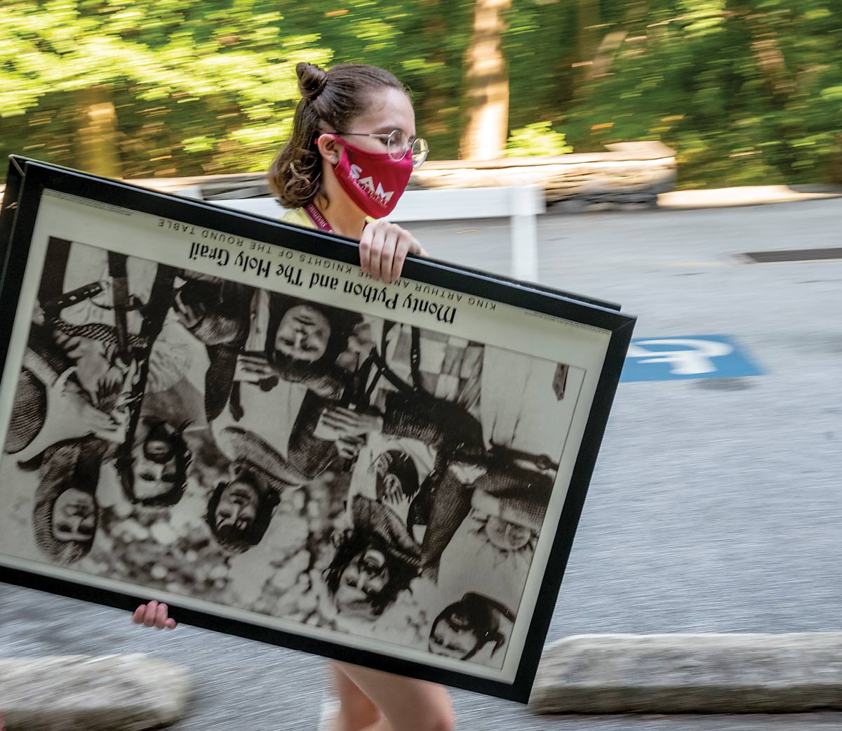 A student wearing a garnet facemask carries and upside-down black-and-white poster of “Monty Python and the Holy Grail”