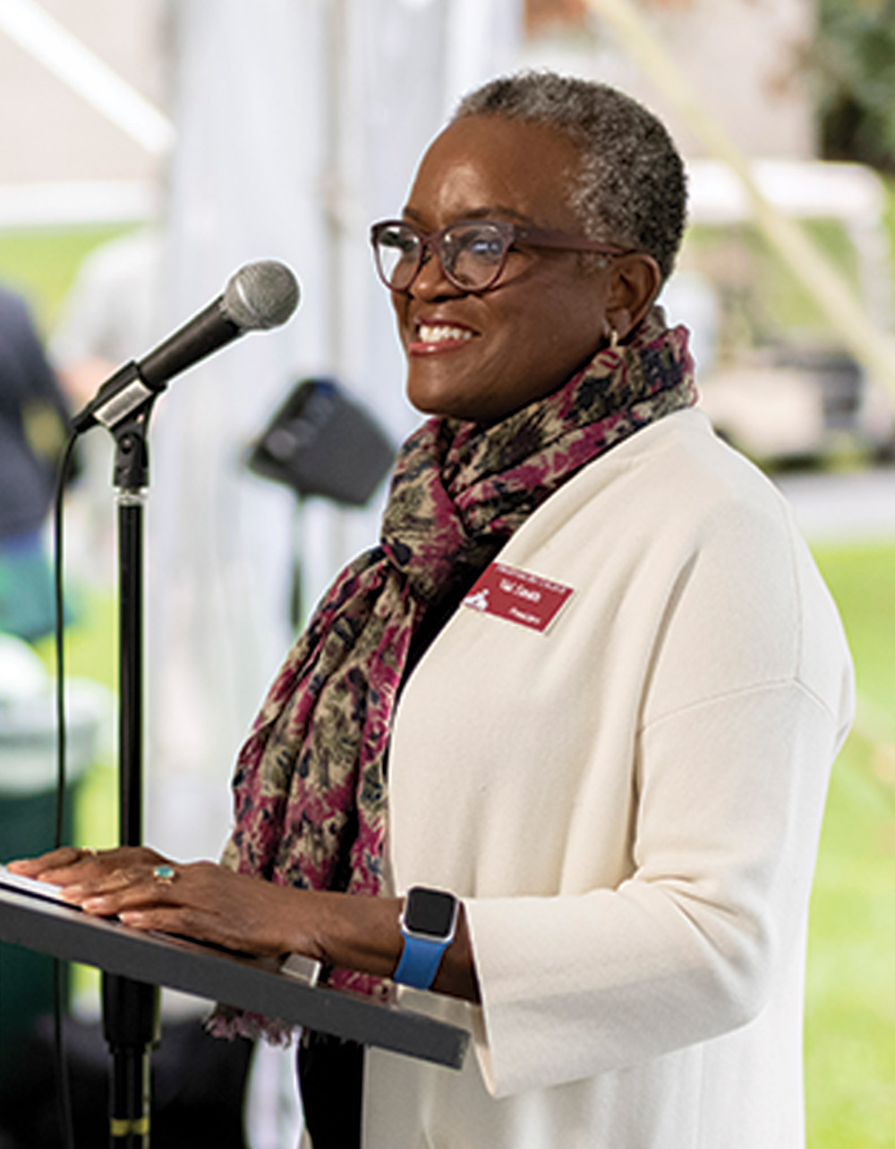 President Valerie Smith, smiling at a lectern and wearing a white sweater and scarf