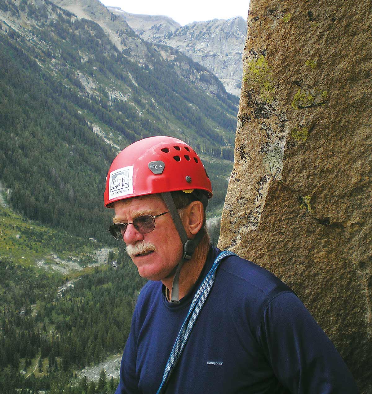 David Thoenen in a red helmet, sunglasses, and a navy shirt, with mountains in the background