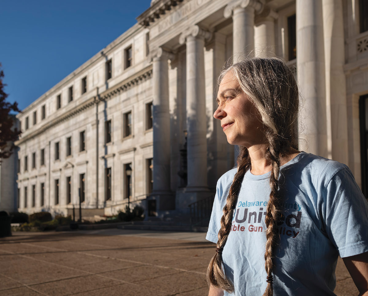 Robin Lasersohn, wearing long braids and a blue t-shirt for Delaware County United For Sensible Gun Policy, standing outside the Delaware County Courthouse