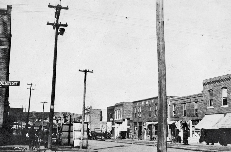 Black-and-white photo of North Greenwood Avenue before the Tulsa race massacre. Telephone poles and tidy shops line a street.