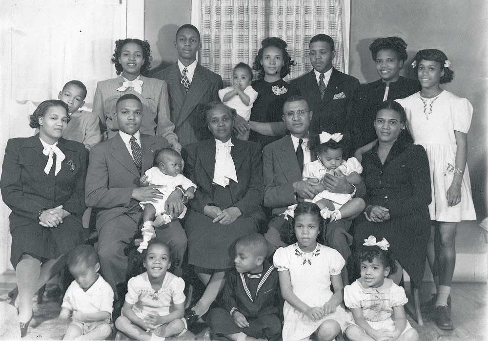 Black-and-white portrait of the Alexander family, ranging in age from infants to grandparents. All are dressed in suits or dresses.