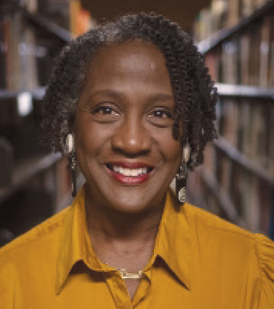 A smiling woman with gold shirt stands in library stacks