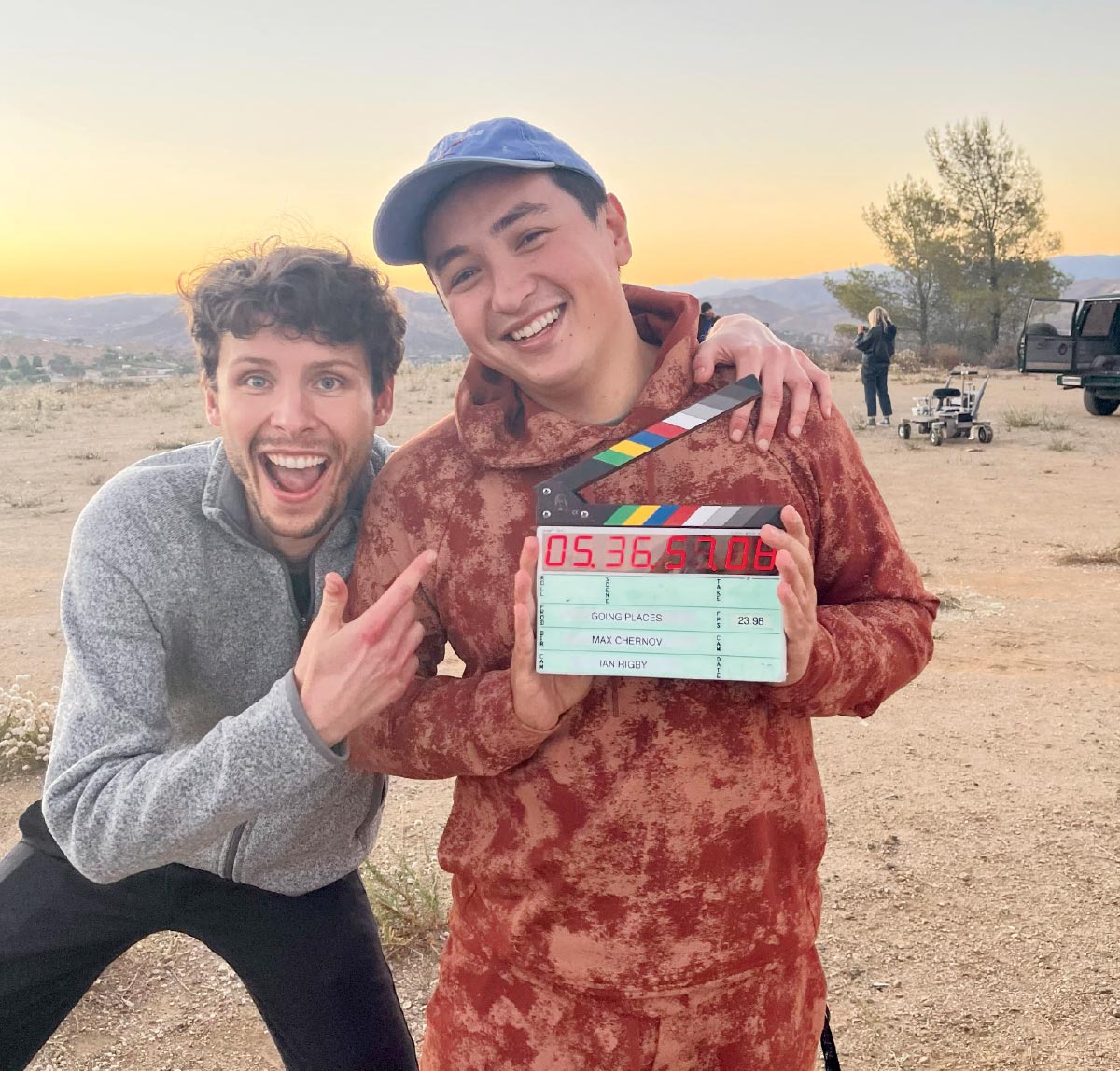 Two young men smile and the desert is in the backgournd. One holds a film clapboard.