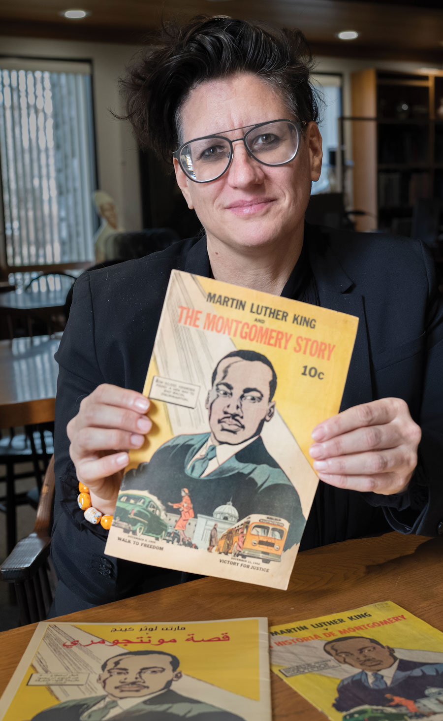 A woman with large glasses and brown hair hold a comic of Martin Luther King Jr. 