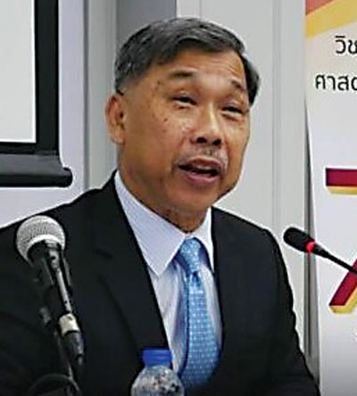 An older man with a suit and tie stands at 2 microphones. 