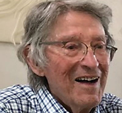 An older man with glasses and a plaid shirt smiles.