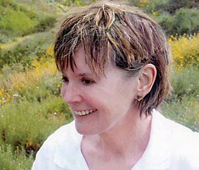A smiling woman with a white shirt, in a field with yellow flowers.