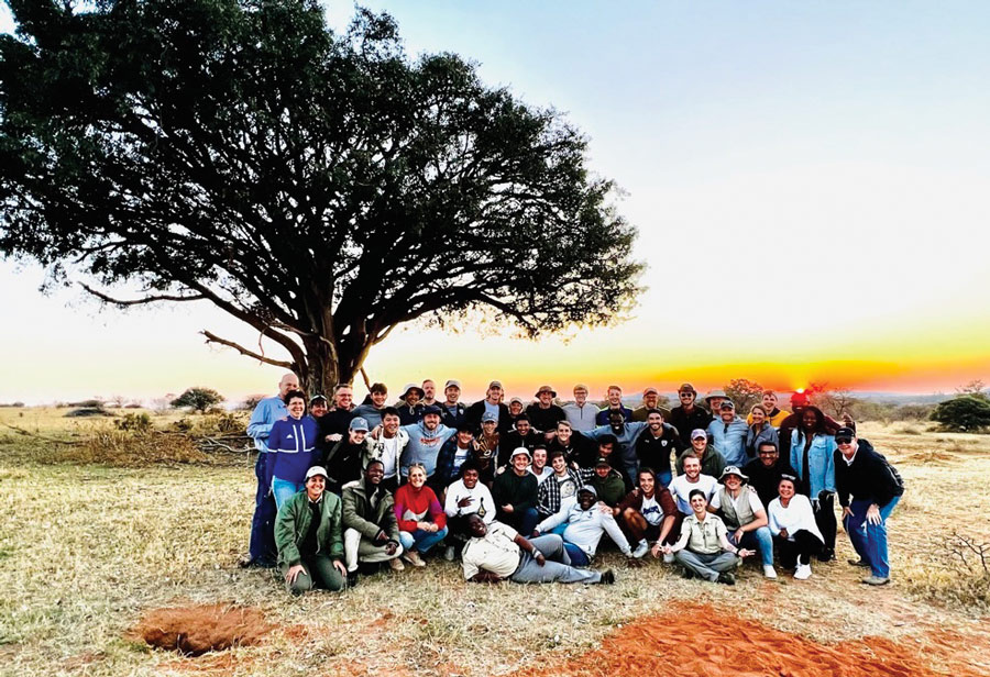 A group of students sit under a tree on a South African plain. The sun sets behind them.