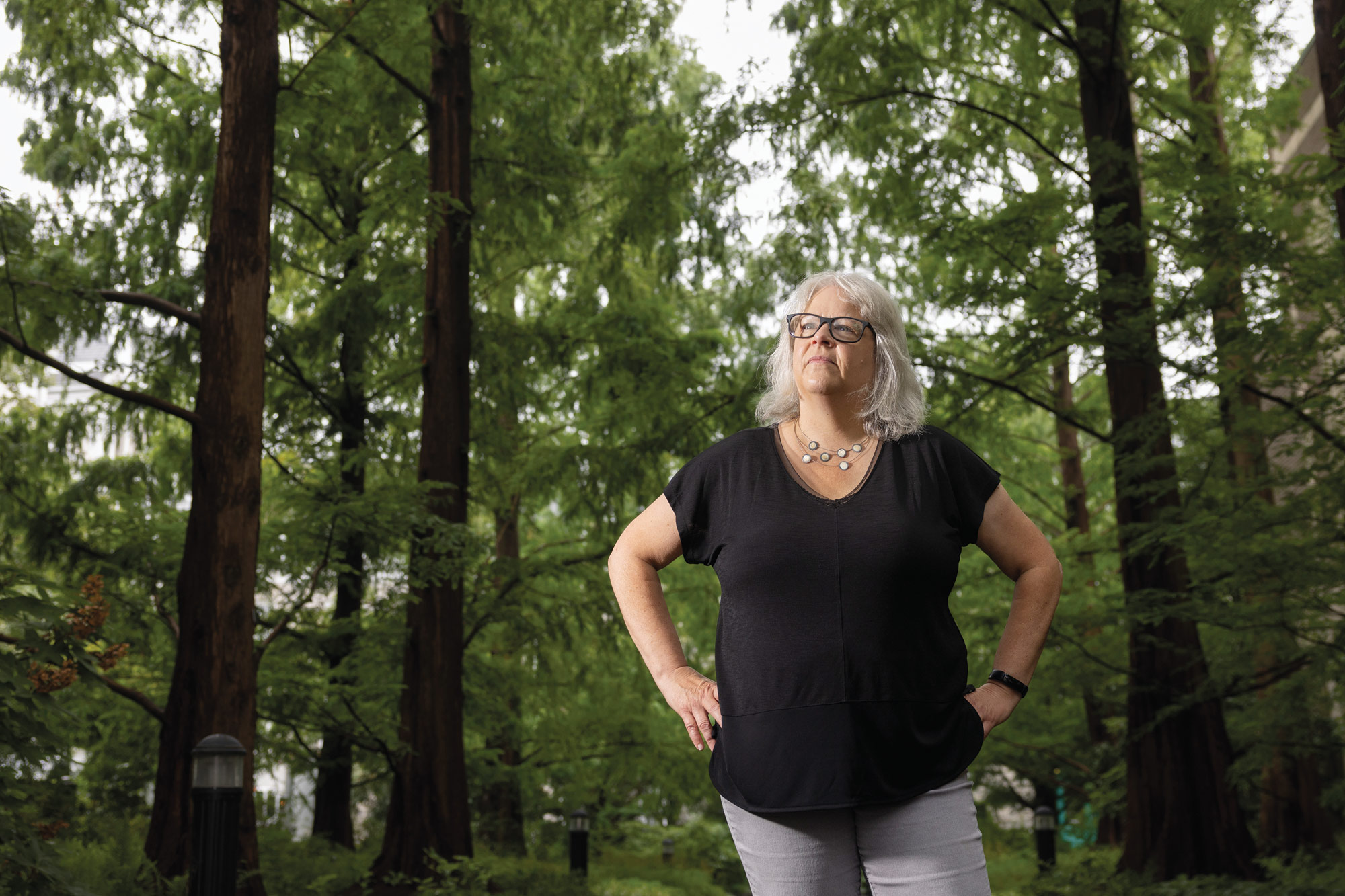 Sunka Simon stands in front of leafy, green trees, looking up and wearing a black t-shirt.