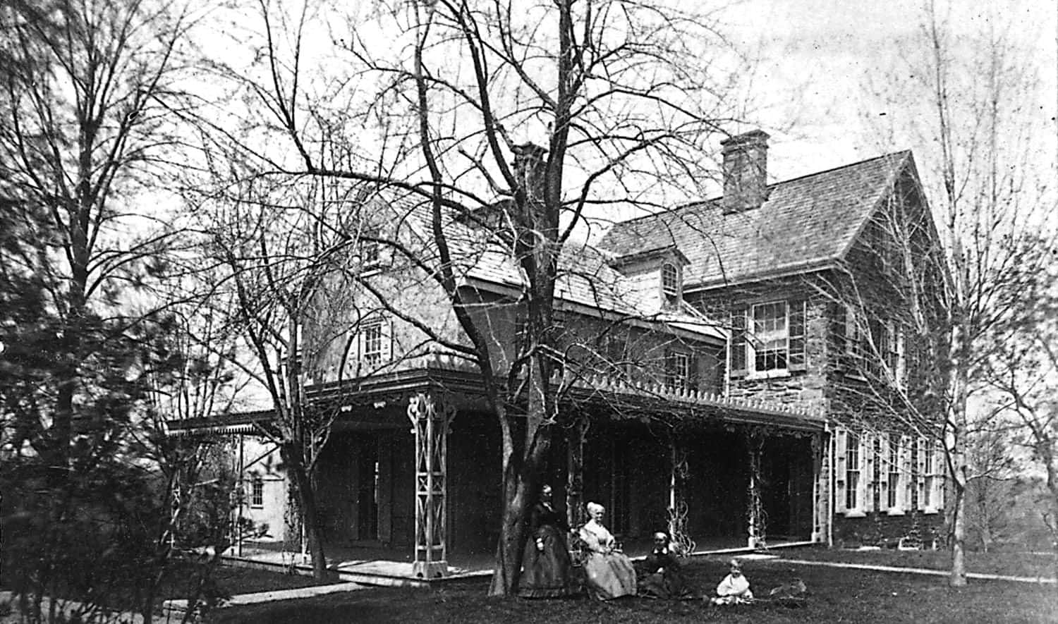 Black and white photo of Lucretia Mott standing in front of a large house with another woman and two children.