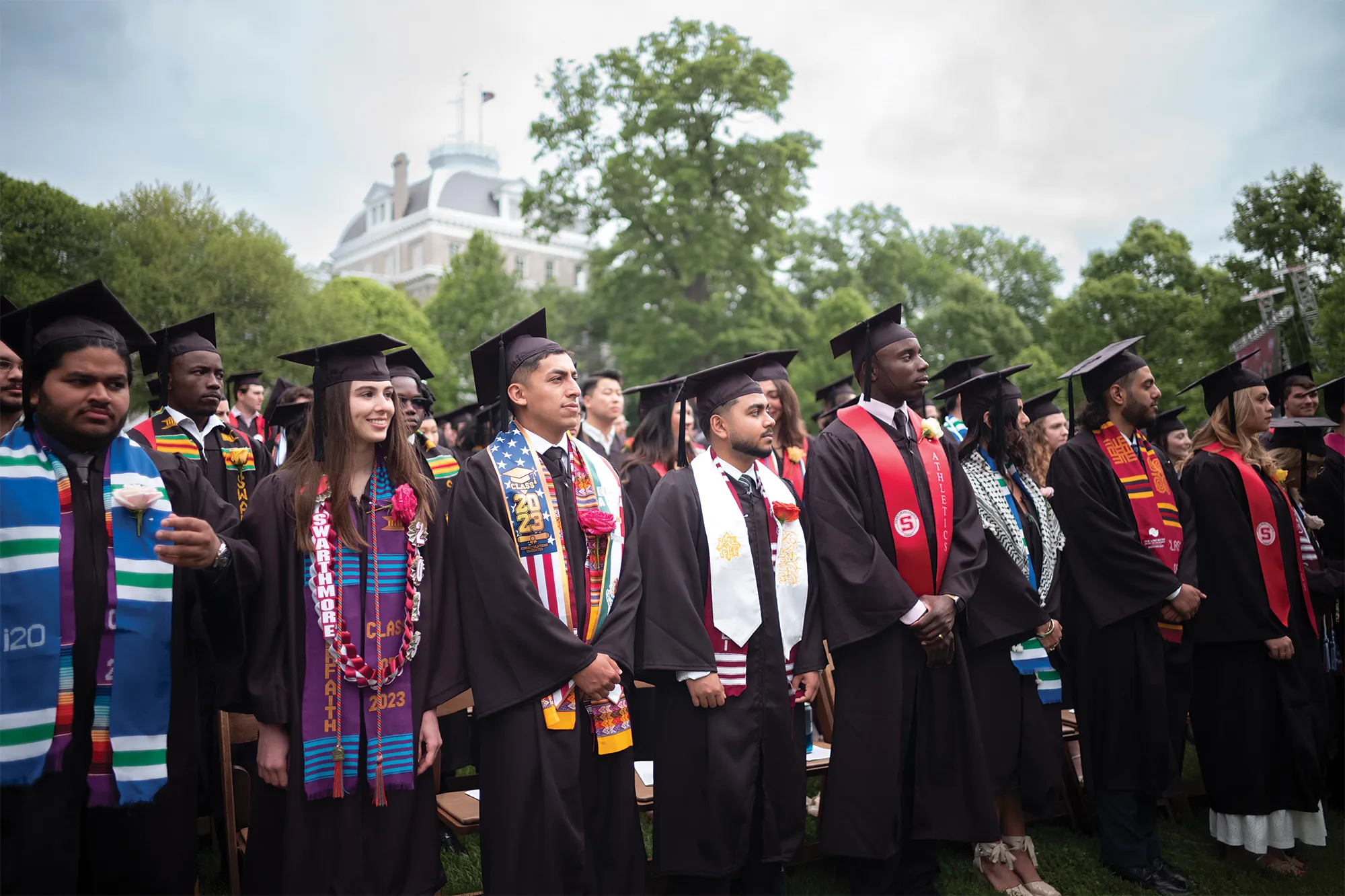 Rows of graduates wearing caps and gowns with Parrish Hall in the background.