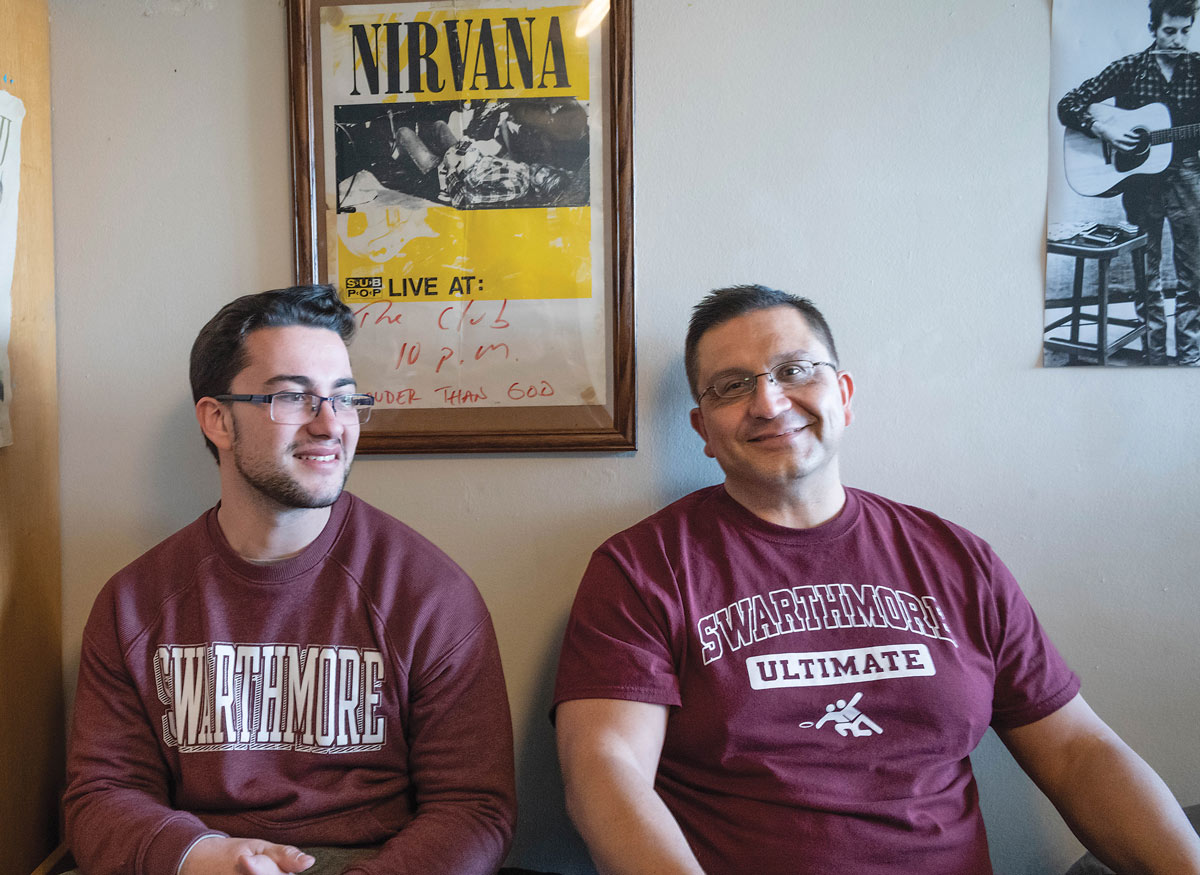 Father and son in Swarthmore shirts sit in dorm room in front of a Nirvana poster.