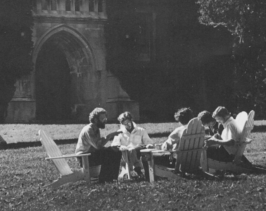 Black and white image of a professor and students sitting in Adirondack chairs in front of Clothier Hall.