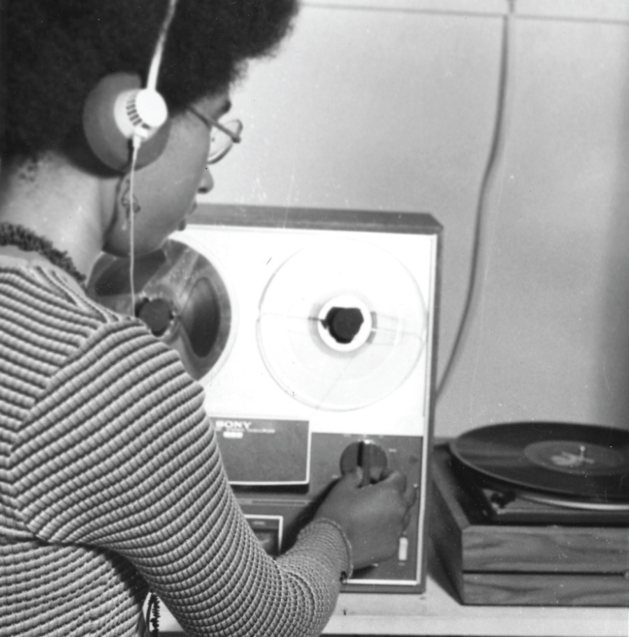 Black and white photo of a student wearing headphones and twisting dials while a vinyl record plays.