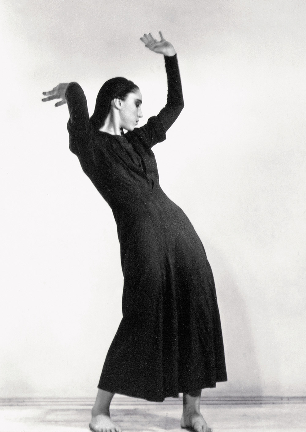 Jane Dudley in "Song of Protest." In this black and white 1937 photo, she wears a long black dress and has both hands in the air.