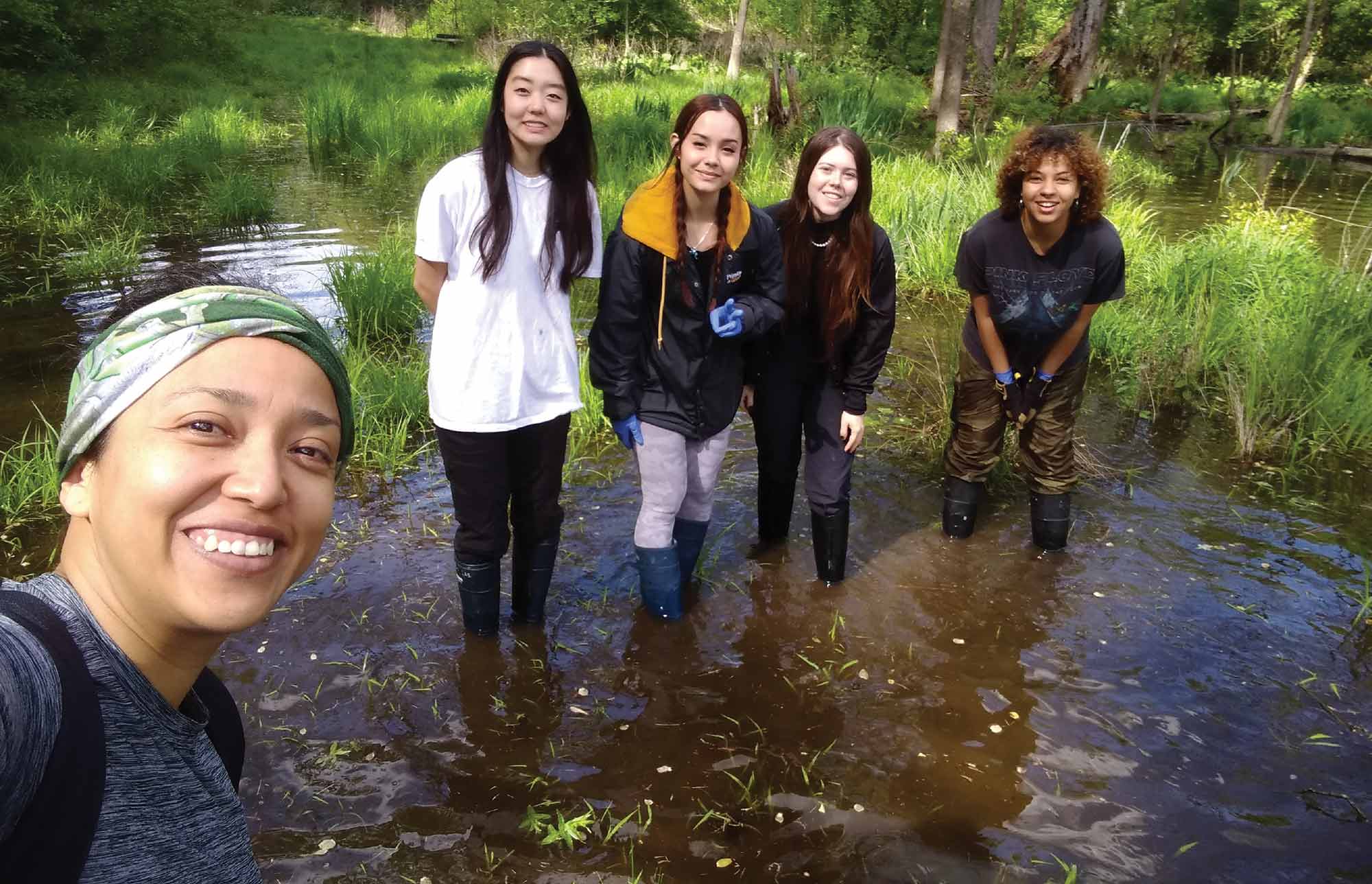 Students in knee-high boots stand in water up to their ankles, conducting research with Associate Professor of biology Itzue Caviedes Solis.