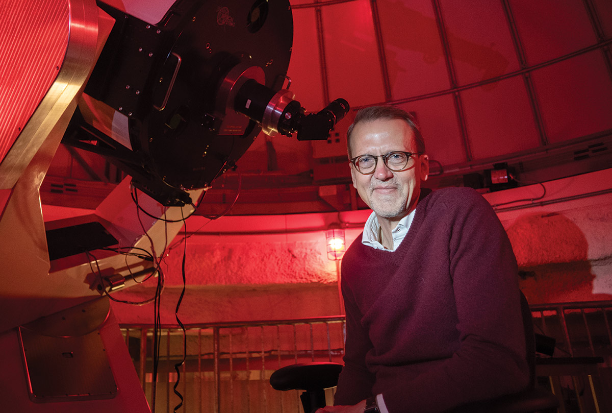 Eric Jensen poses with a giant telescope in a red-tinted observatory.