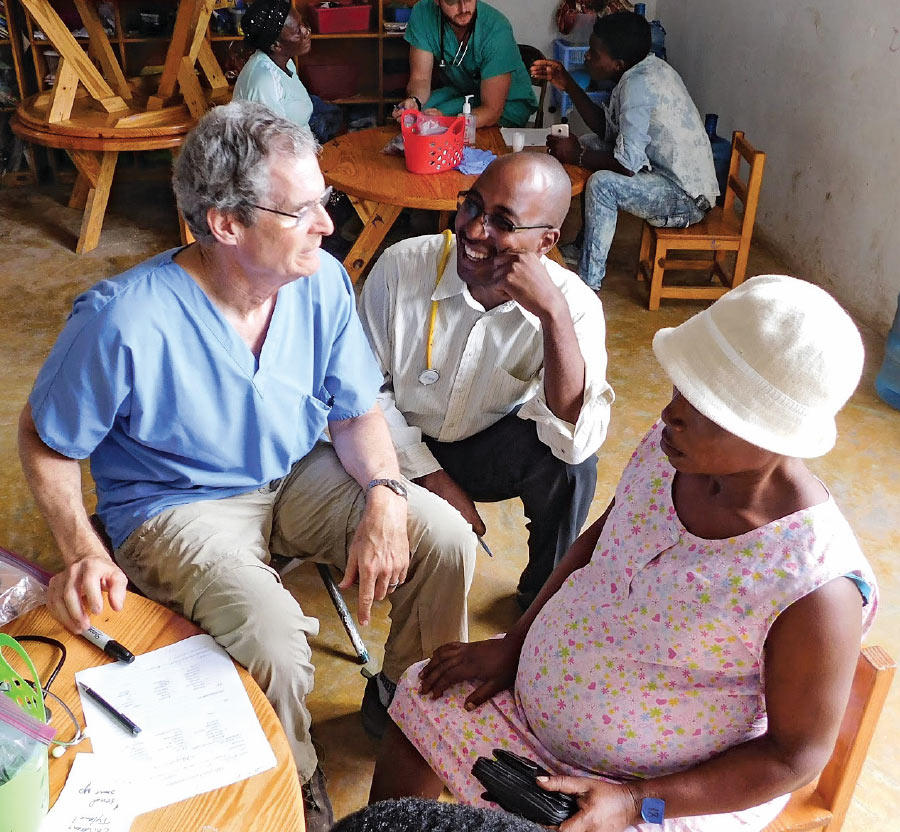 Neil Heskel sitting with a colleague and a patient at the Haiti Clinic.