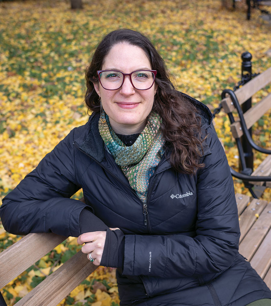 Amy Kapit '06 sits on a bench with fall leaves behind her.