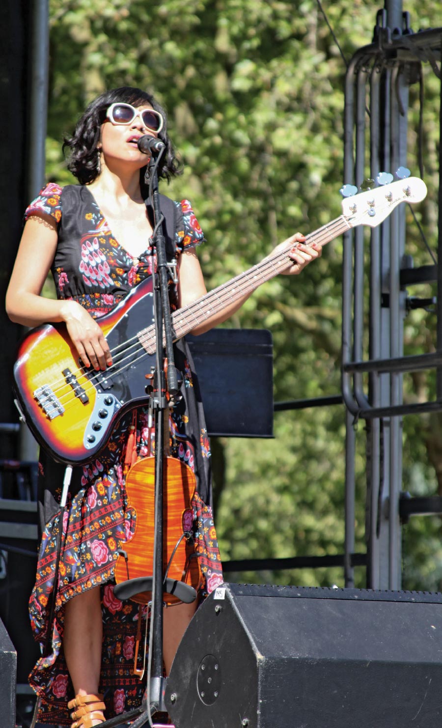 Hsu performing onstage at an outdoor festival, wearing a colorful dress, sandals, and sunglasses.