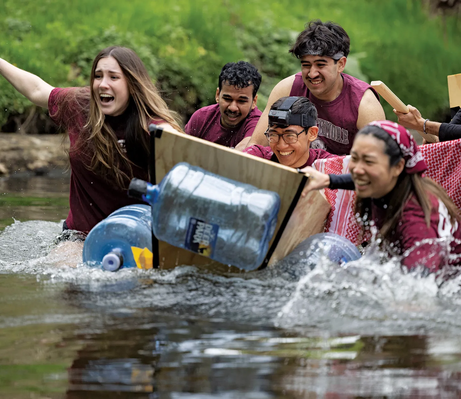 Smiling students attempt to race a vessel they built out of wooden planks and large plastic water jugs down Crum Creek.