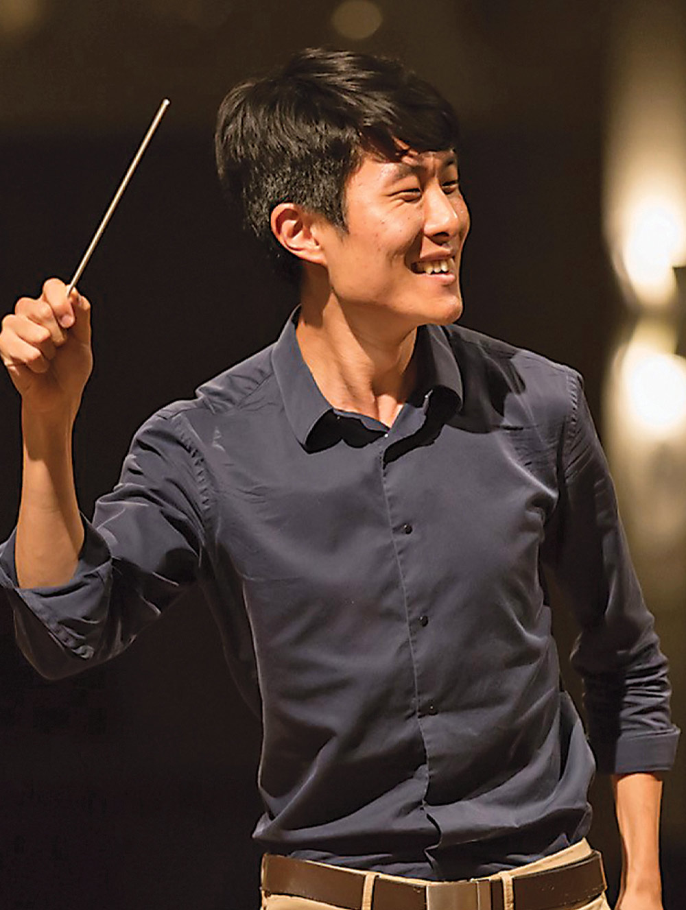 Color photo of Andrew Kim smiling while conducting music with a baton.