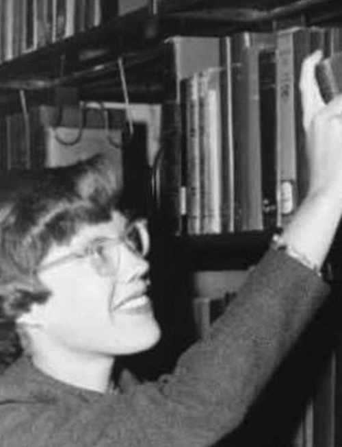 Elizabeth "Peggy" Brown '54 pulls a book off a shelf in a black and white photo