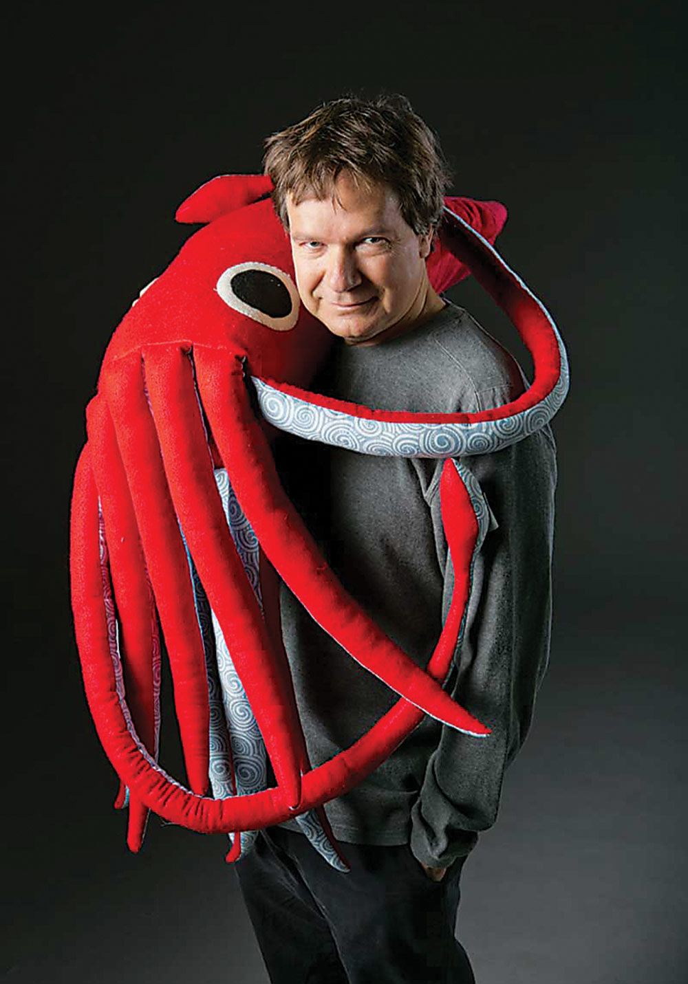 Sönke Johnson stands looking at the camera, embraced by a red squid-shaped stuffed animal.