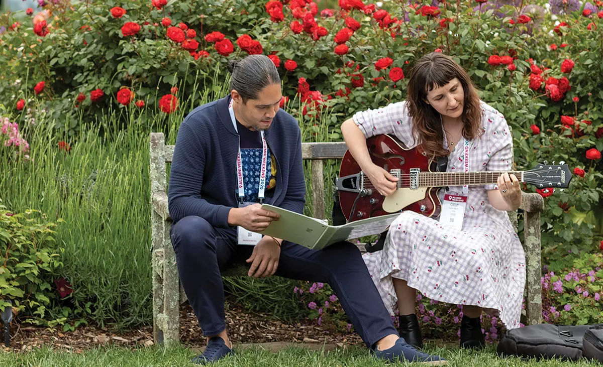 Alumni making music on a bench outside.
