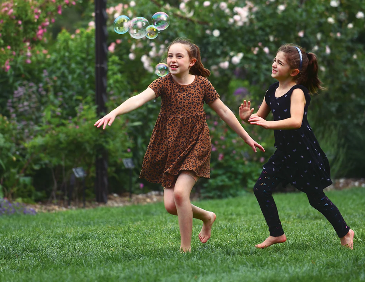 Children chase bubbles across the lawn