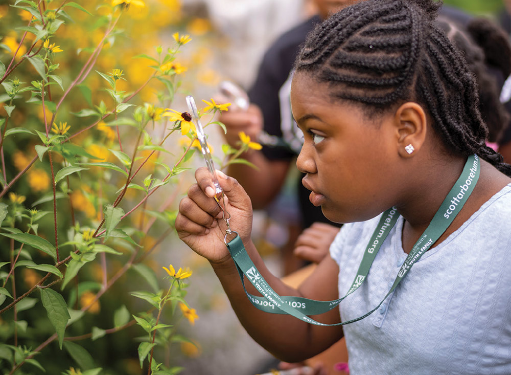 Messiah Muhammad examines a plant through a magnifying glass.