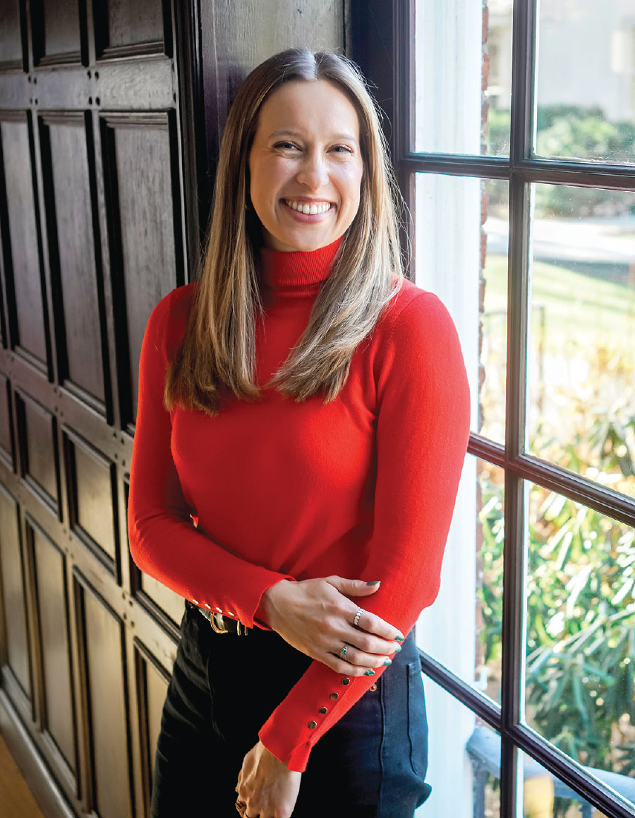 Bridget Silveria '20 wears a bright red turtleneck and stands by a window.