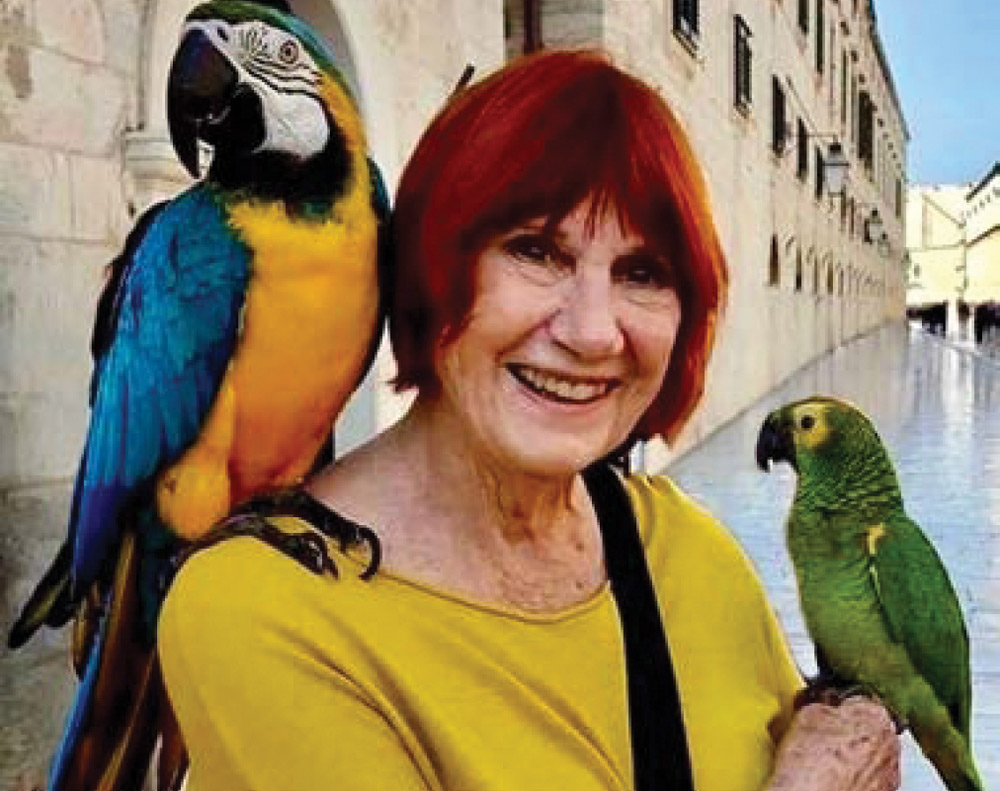 Joan Pallme Bassin '60 head shot with a blue and yellow parrot and a green parakeet