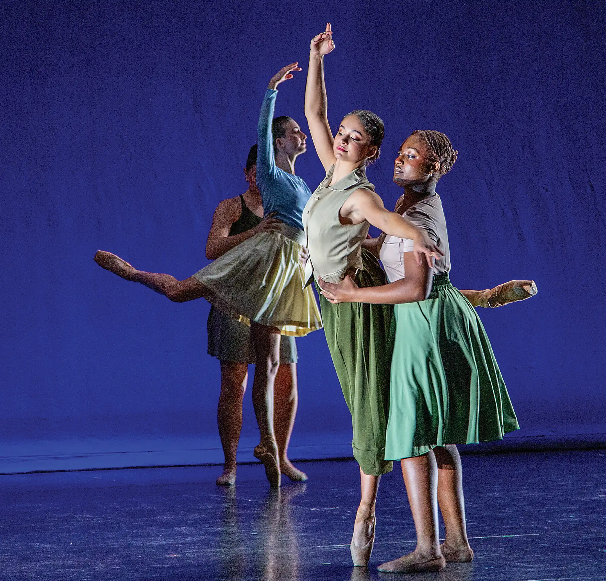 Dancers perform ballet in green costumes in front of a dark blue backdrop.