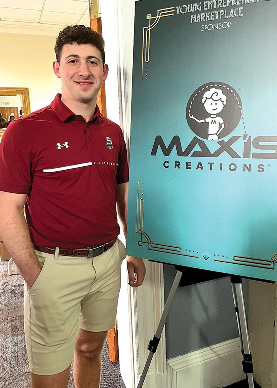 Max Ash '27 stands by a sign advertising Max'is Creations.