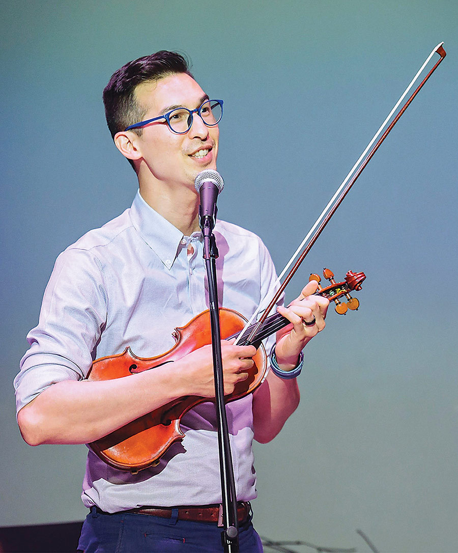 Wren Elhai '08 holds a violin and speaks into a microphone.